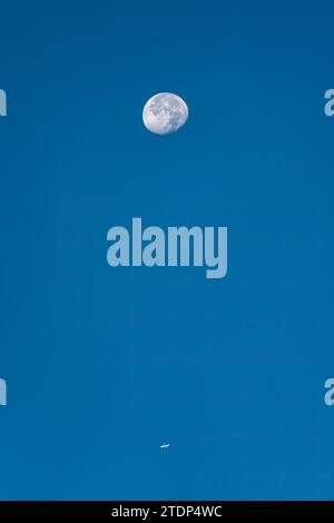 Big Moon and small airplane against clear blue sky in daytime Stock Photo