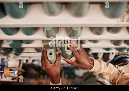 Above view of hands of young African American shoemaker taking workpieces of footwear from shelf before starting work Stock Photo