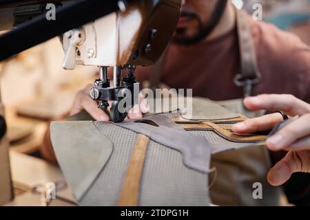Close-up of young shoemaker or tanner using sewing machine while processing piece of grey suede and creating new items Stock Photo