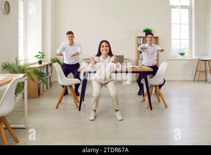 Happy young company employees doing sit-ups exercises in office on their workplace. Stock Photo