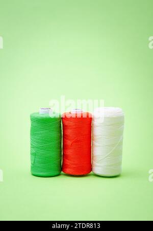 Various spools of sewing cotton thread of different colors italian flag on green background Stock Photo