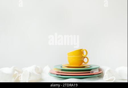 The image has a bright and minimalistic setting. A cup and saucer are placed on top of a stack of colorful plates - green and pink tones are visible Stock Photo