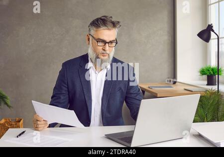 Portrait of middle aged businessman working with laptop and papers on desk Stock Photo