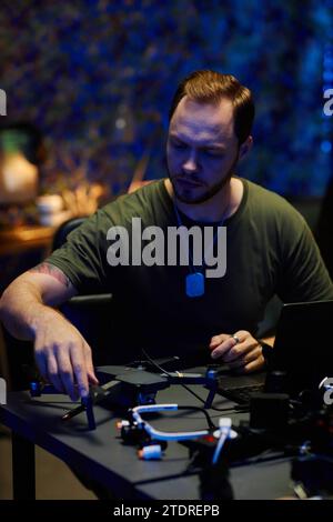 Young military officer constructing or repairing drone while sitting by workplace and fixing together details of device Stock Photo
