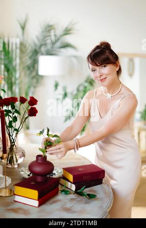 Close up of bouquet arrangement. Woman puts roses in vase on table at home. Fresh red blooms. Interior and decor. Stock Photo