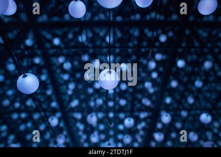 Many light bulbs that go down with their cables from the ceiling creating a unique optical illusion. abstract lighting perspective view in blue color Stock Photo