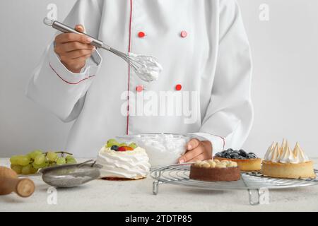 Female confectioner cooking tasty cakes on white background Stock Photo