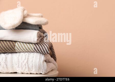 Stack of folded sweaters with gloves on stool against beige background Stock Photo