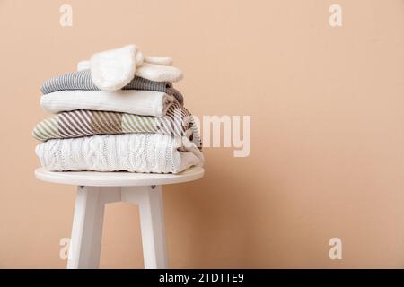 Stack of folded sweaters with gloves on stool against beige background Stock Photo