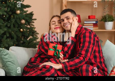 Young couple wearing plaid pajamas with gift in living room decorated for Christmas Stock Photo
