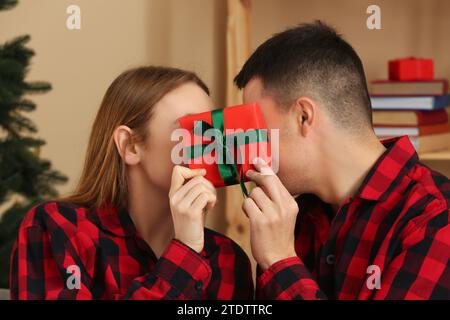 Young couple wearing plaid pajamas with gift in living room decorated for Christmas Stock Photo