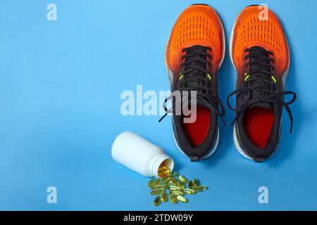 Orange sports sneakers, vitamin E and D capsule tablets spilled out of a jar on a blue background with copy space Stock Photo