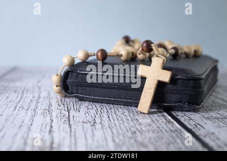 Rosary with cross laying on old Holy Bible book on rustic wooden table. Christianity, religion, religious symbol. Prayer Stock Photo