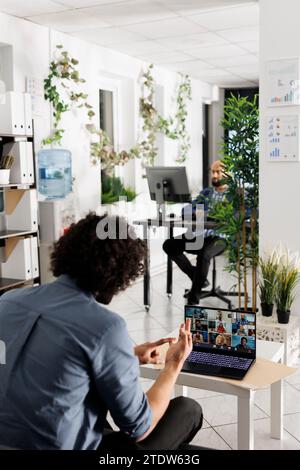 Project manager communicating with coworkers via video call to discuss work progress. Employees team talking about company growth strategy in online meeting using laptop in office Stock Photo