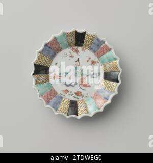 Saucer with a woman in a garden and diaper patterns on various colored grounds, anonymous, c. 1725 - c. 1749 Porcelain dish with ribbed wall and scalloped edge, painted on the glaze in blue, red, pink, green, yellow, black and gold. On the flat of the dish a woman (long lijs) sitting on a rock in a fenced garden with flowering plants; The edge divided into narrow compartments with servetwork on different colored backgrounds. Famle Rose. China porcelain. glaze. gold (metal) painting / gilding / vitrification Porcelain dish with ribbed wall and scalloped edge, painted on the glaze in blue, red, Stock Photo