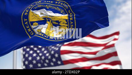 Nebraska state flag waving with the American flag in background on a clear day. Dark blue with a large state seal of Nebraska at its center. 3d illust Stock Photo