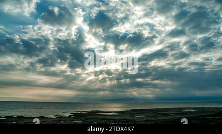 The sunrise on Gili Island looks like a stretch of beach and coral rocks with dramatic clouds Stock Photo