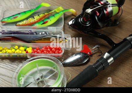 Fishing rod with spinning reel and baits on wooden background, closeup Stock Photo