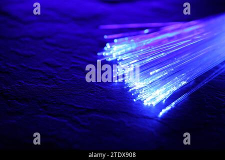 Optical fiber strands transmitting color light on textured background, closeup. Space for text Stock Photo