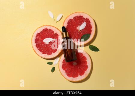 Bottle of cosmetic serum, grapefruit slices and green leaves on wet yellow background, flat lay Stock Photo