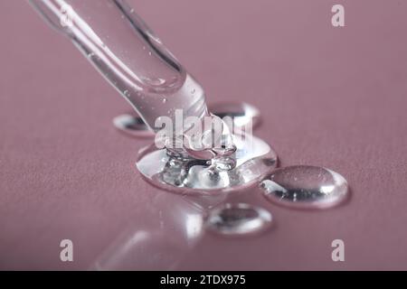 Dripping cosmetic serum from pipette onto pink background, macro view Stock Photo