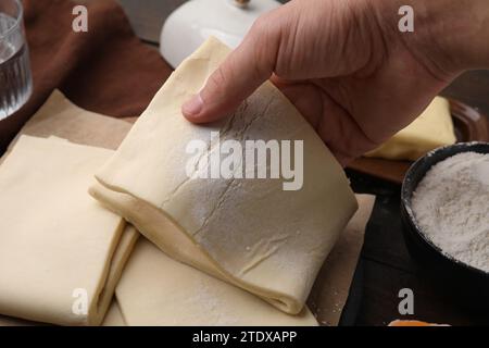 Man holding raw puff pastry dough at wooden table, closeup Stock Photo