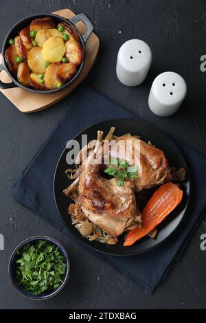 Tasty cooked rabbit meat with vegetables and potato served on black table, flat lay Stock Photo