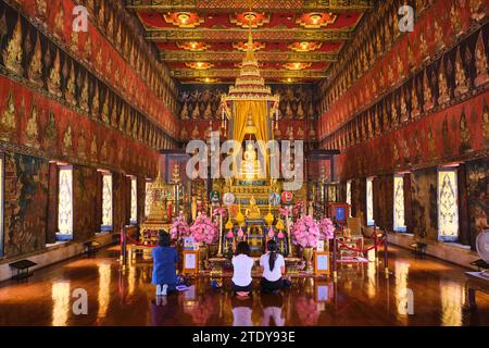 A few kneeling worshippers, busy praying. Inside the red, richly decorated Buddhaisawan Hall Buddhist temple. At the National Museum in Bangkok, Thail Stock Photo