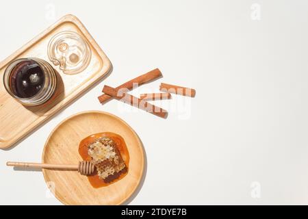 Honey is stored in a glass jar on a wooden tray, natural raw beeswax and a honey drizzle on a wooden plate, next to cinnamon. Space for product displa Stock Photo