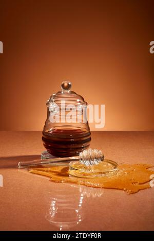 Front view of a glass jar containing honey, honey scattered on a brown background with glassware. Honey can be made into medicine to heal wounds. Stock Photo