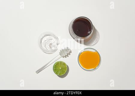 Honey is served in glass containers and half a lemon is displayed on a white background. Natural ingredients to make tea to support health. Top view. Stock Photo