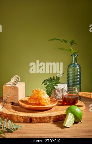 Natural raw beeswax on wooden plate, honey in beaker, surrounded by decorations on wooden table with moss green background. Concept of honey and healt Stock Photo