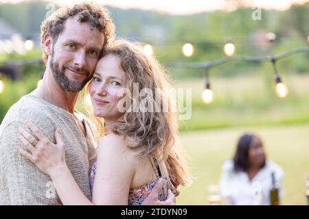 Smiling couple embracing at an outdoor garden party with string lights Stock Photo