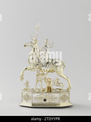Table automaton in the form of Diana on a stag, Jacob Miller (edelsmid), c. 1613 - c. 1615 Diana, seated on a deer. Silver automatic, partially gilded. The deer, which has a removable head and carries a crown, is surrounded by open -up band ornament. Similar decorations around the eight -sided pedestal, on which all kinds of insects and animals are placed on a natural soil, including two hunting dogs, a rider and a hunter. A few holes indicate other, lost additions. Diana looks back. She wears an arc and a arrow sleeve on the back and holds the end of the chain in her raised left hand, with wh Stock Photo