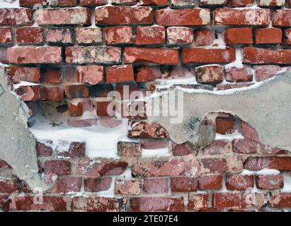 damaged plaster on red brick wall in winter Stock Photo