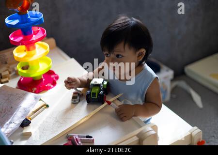 Adorable Boy Sitting On Table Drawing On Paper At Home.  little toddler boy  draws with Crayons in the paper in the children's room at home. Education Stock Photo