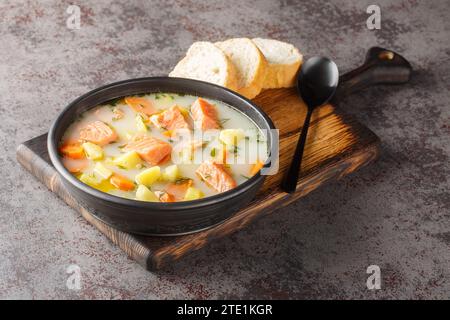 Lohikeitto, salmon fish soup with cream, potato, carrots, leek and dill closeup in a bowl on the serving board. Horizontal Stock Photo