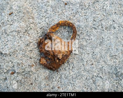 A rusty old padlock that has lain at the bottom of the river for many years on a flat granite stone. Background Stock Photo