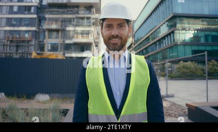 City urban building construction industry work Caucasian middle-aged adult man worker in hardhat happy smile male contractor engineer in helmet vest Stock Photo