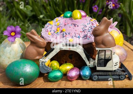 model of a toy excavator, Easter cake, chocolate bunnies with bright multi-colored eggs. Stock Photo