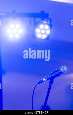 Dynamic stage ambiance: Blue-lit microphone on stand, set against vibrant stage lights. Captures live performance energy. Stock Photo