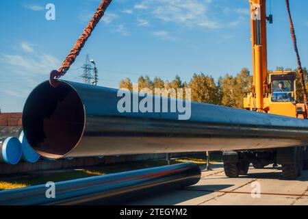 Shipment of new large diameter metal pipes on summer day from open warehouse. Tractor lift unloads pipes for gasification. Industrial background for gas equipment supplier. Stock Photo
