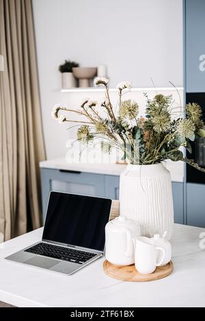 Home Office Setup with Laptop and Cozy Kitchen Decor. A chic home office setup featuring an open laptop on a marble countertop, complemented by a warm Stock Photo