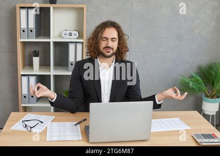 Young relaxed business man meditating and having a rest in the office on his workplace. Stock Photo