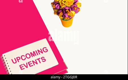 UPCOMING EVENTS are written in pink on a notepad. Pink folder and flower on a white background. Stock Photo