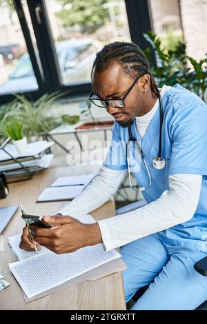 confused african american doctor with glasses taking notes and consulting by phone, telehealth Stock Photo