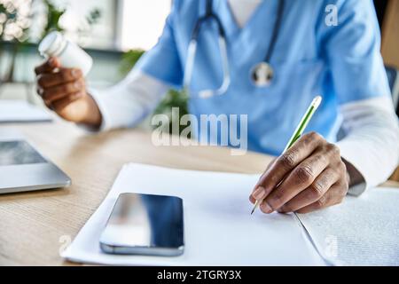 cropped view of african american doctor with stethoscope taking notes while working, phone on table Stock Photo