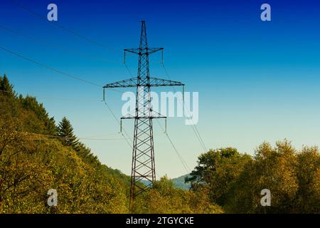 High-voltage power line against the background of the blue sky in autumn in the mountains. Metal wires on a high-voltage tower transmit electricity lo Stock Photo
