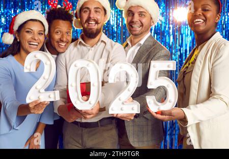 Group of happy colleagues with numbers 2024 celebrating New Year and having fun at party Stock Photo