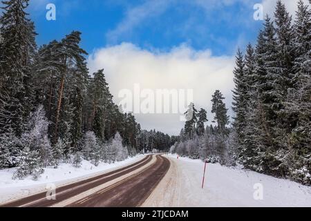 Beautiful view of winter landscape with road passing through forest against backdrop of blue sky with white clouds on frosty day. Sweden. Stock Photo
